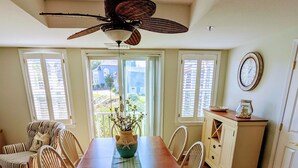 A dining room with a wooden table, chairs, a ceiling fan, and a view of the outdoors through large windows. - Unique Waterfront Condo at the Boatyard! (Kennebunk)
