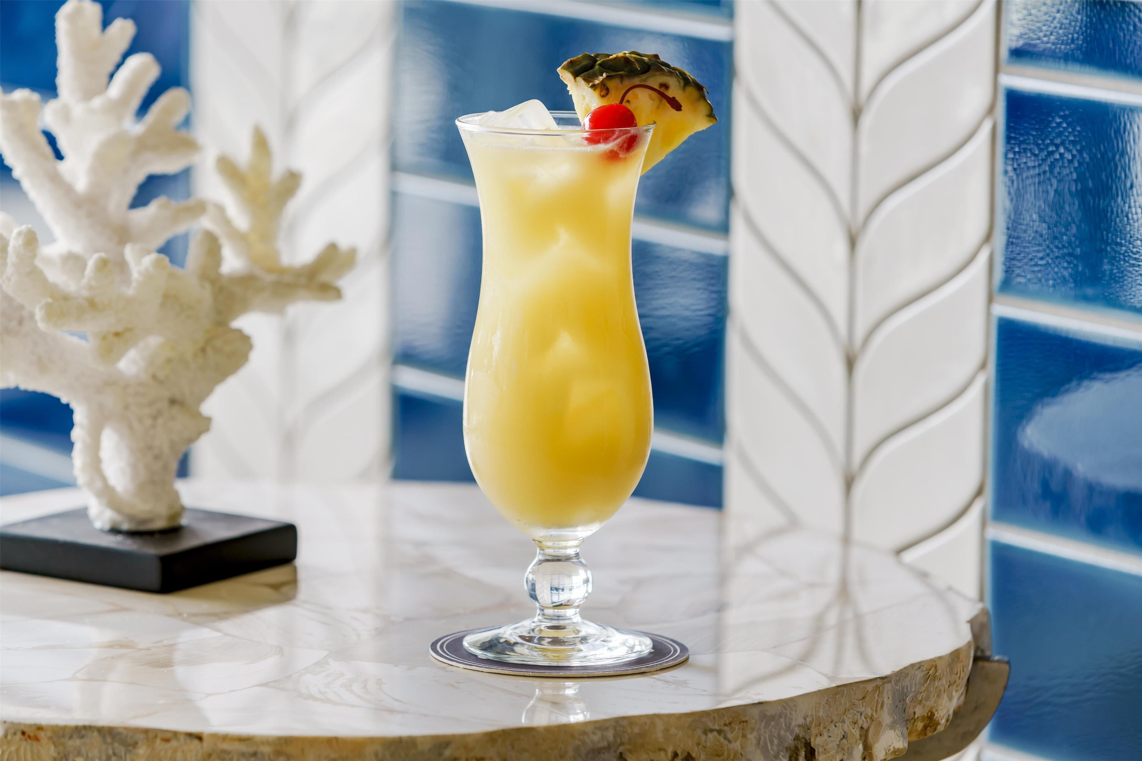 Un cocktail servi dans un verre, décoré d’un morceau d’ananas, posé sur une surface en marbre.