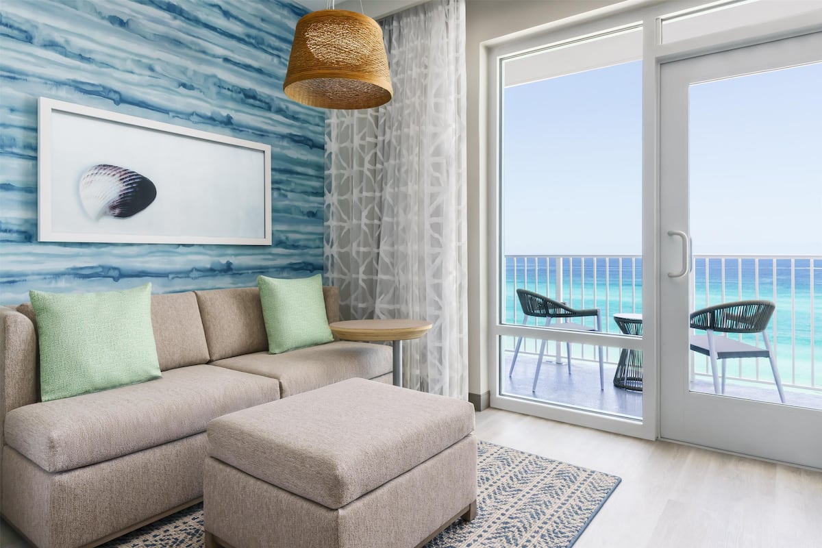 A modern living room with a sofa, ottoman, and a framed seashell artwork on the wall.