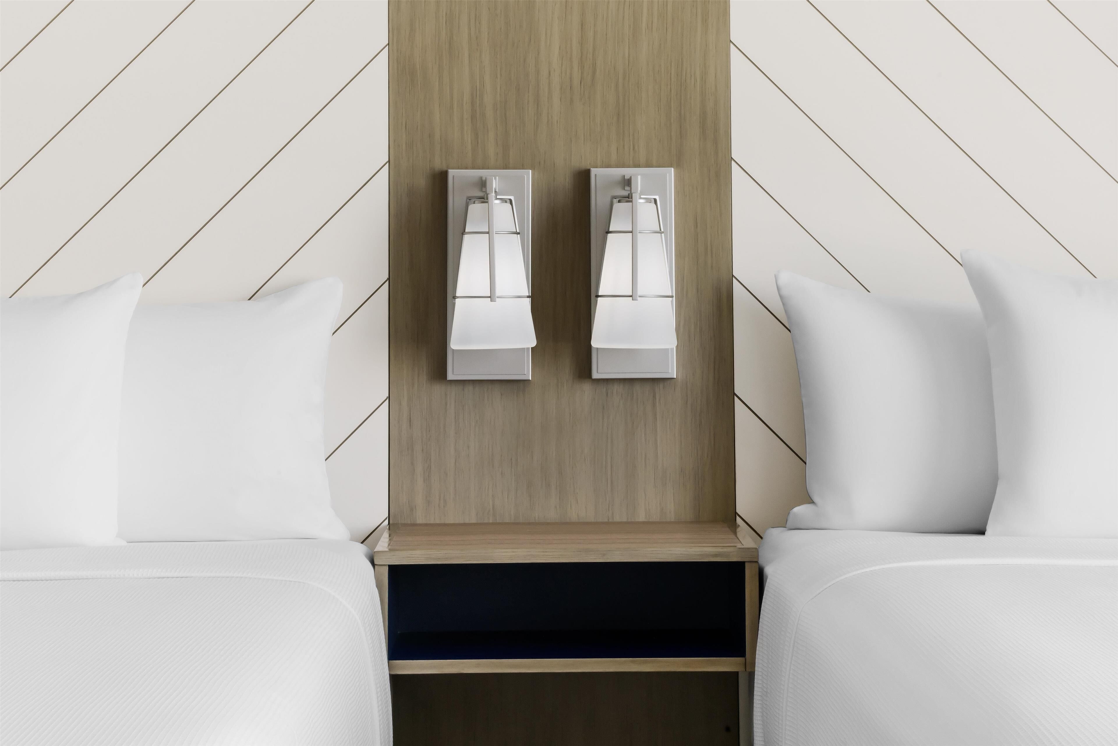 Ein Hotelzimmer mit zwei Betten, einem Holzkopfteil und Wandleuchten.