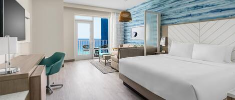A hotel room with a large bed, a desk with a chair, a TV, and a view of the ocean.