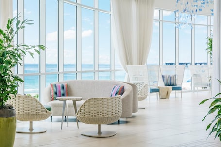 A spacious room with large windows, a white sofa, wicker chairs, and a small table.. Hyatt Place Panama City Beach