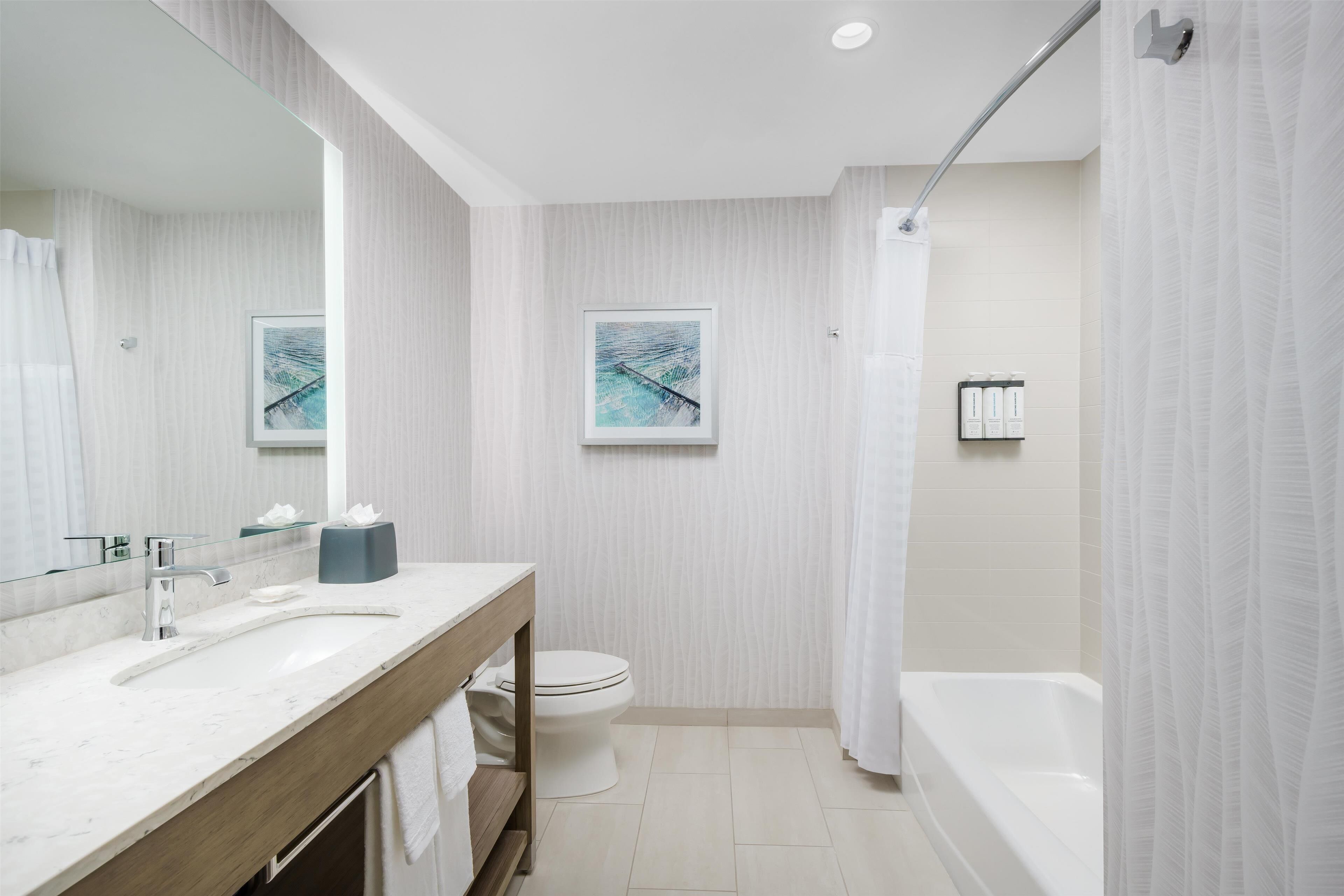 A modern bathroom with a marble sink, a toilet, a bathtub, and two framed artworks on the wall.