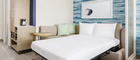 A hotel room with a bed, a sofa, a coffee machine, and a wall with a framed picture.