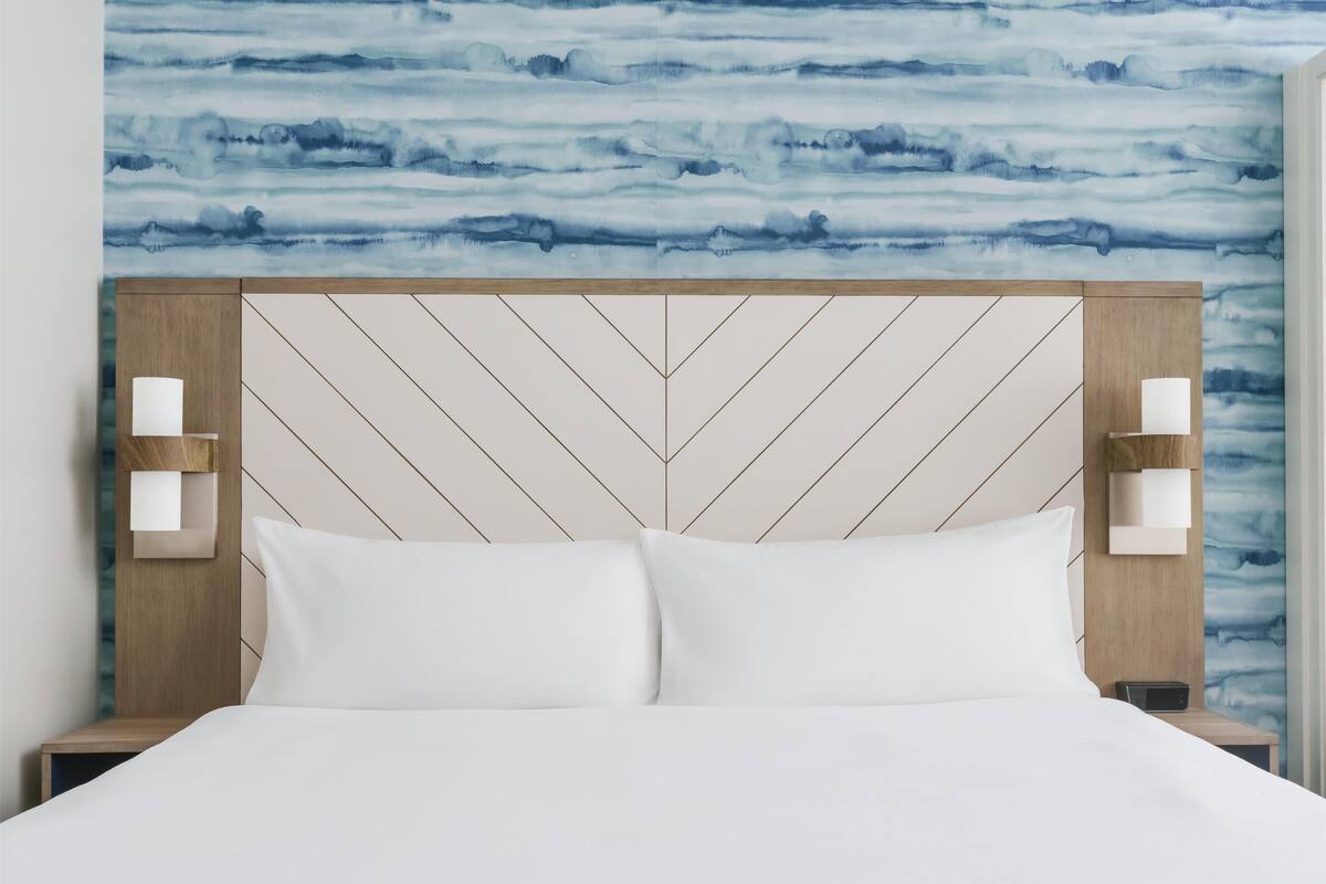 A bed with a wooden headboard, white bedding, and a wall with a blue abstract pattern.