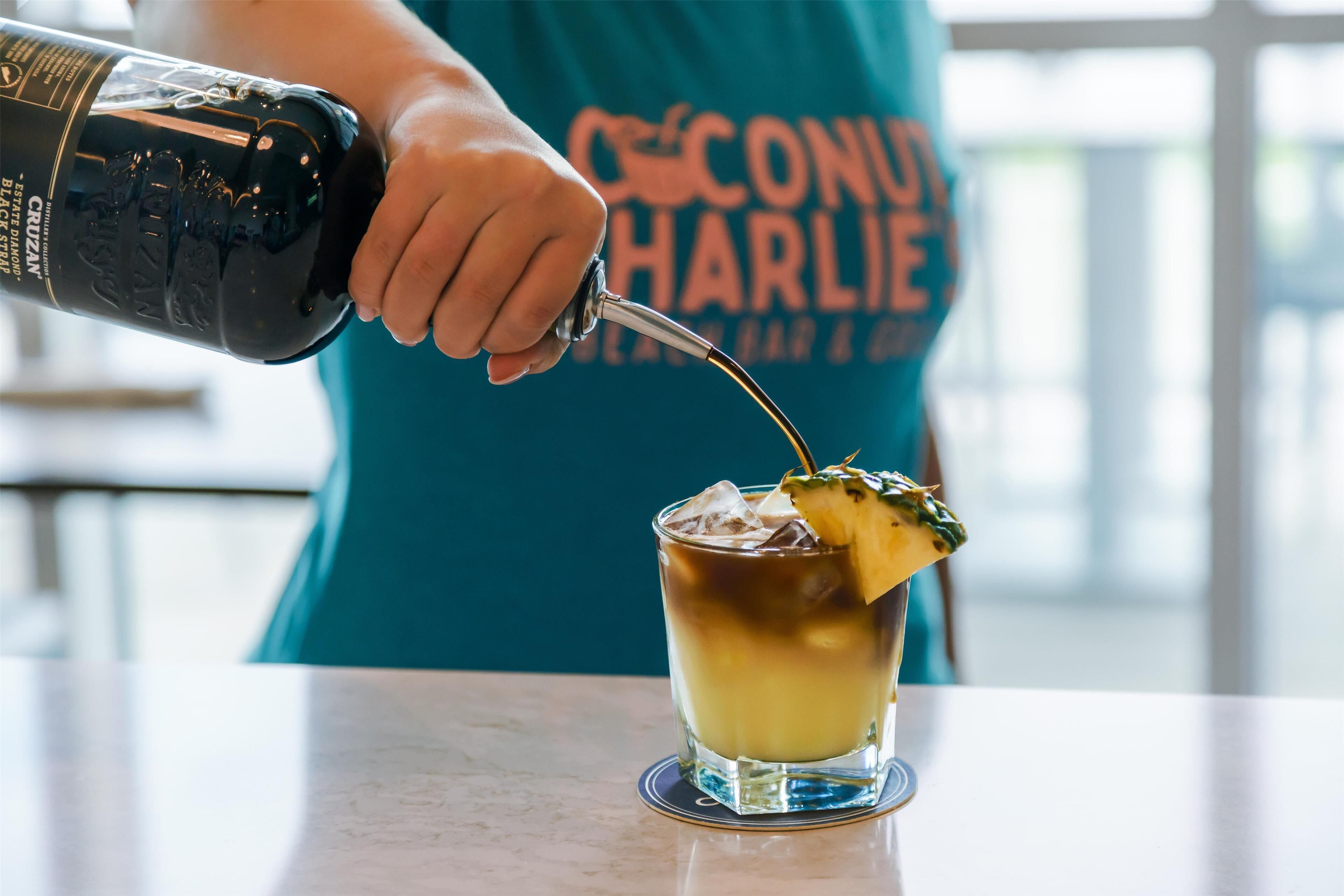 Iemand giet een drankje in een glas met een ananasdecoratie.