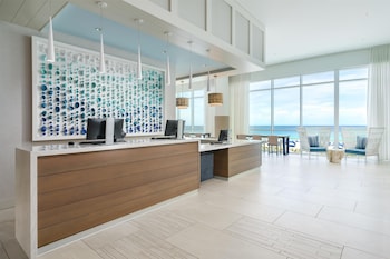 A hotel room with a large bed, a TV mounted on the wall, a wooden dresser, and a view of the ocean. at Hyatt Place Panama City Beach