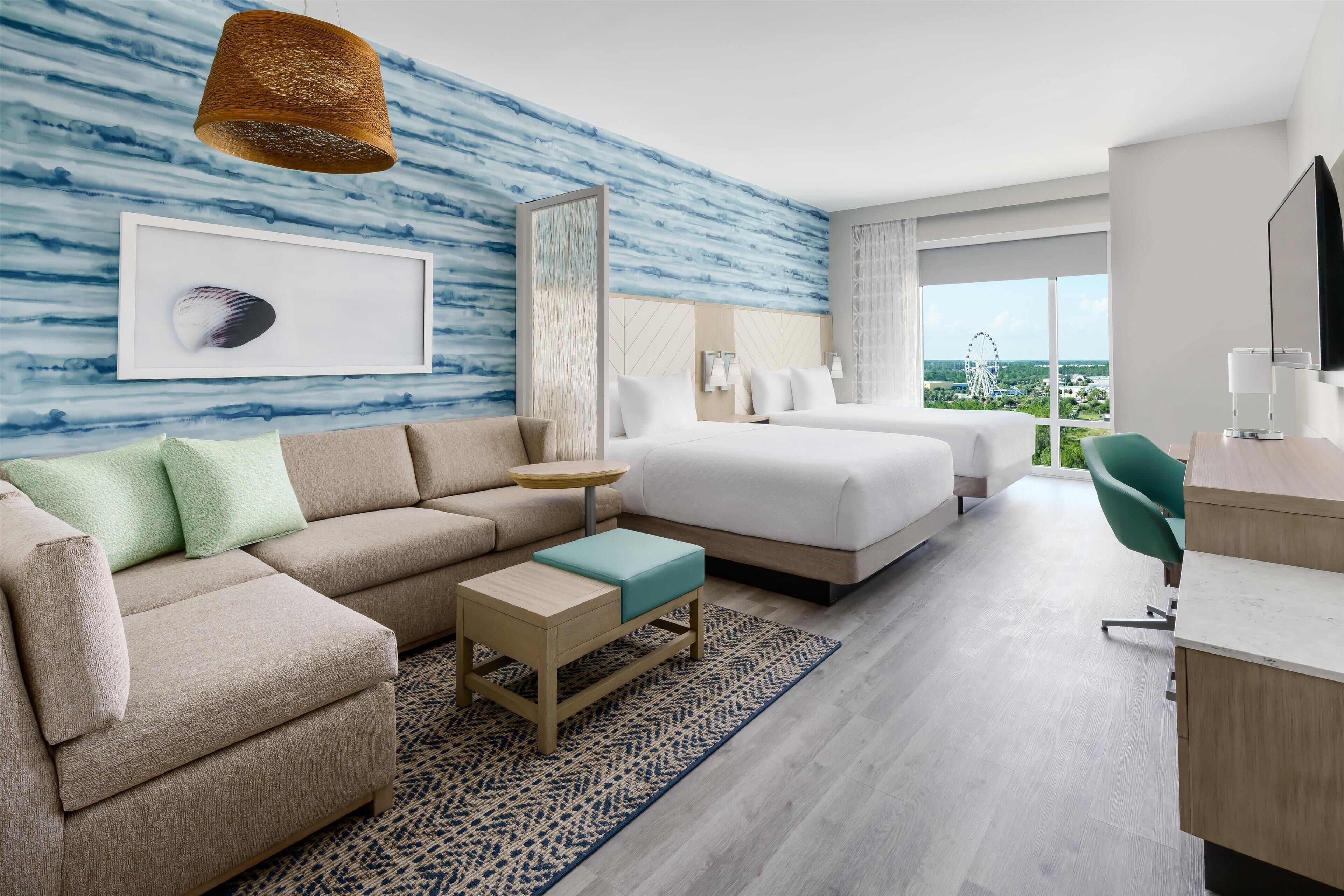 A modern hotel room with a large bed, a sofa, a desk, and a view of a Ferris wheel.