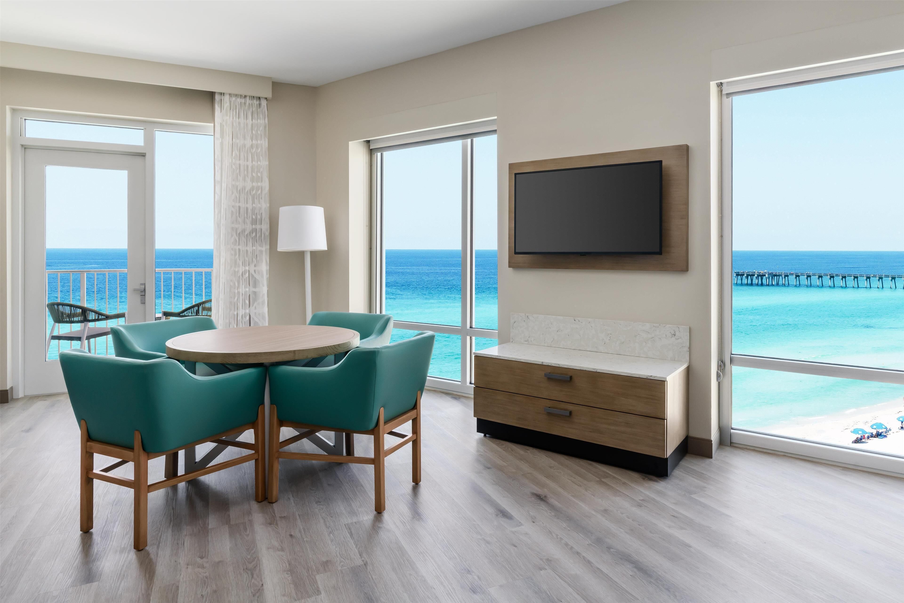 Una habitación moderna con una mesa redonda, sillas color turquesa, un armario de madera y un televisor en la pared.