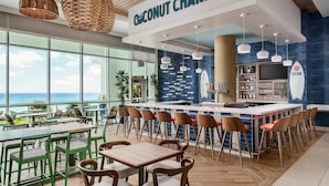 A modern bar area with a view of the ocean, featuring a bar counter, stools, and a sign reading "Coconut Charlie's". - Hyatt Place Panama City Beach (Panama City Beach)