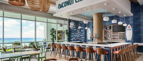 A modern bar area with a view of the ocean, featuring a bar counter, stools, and a sign reading "Coconut Charlie's".