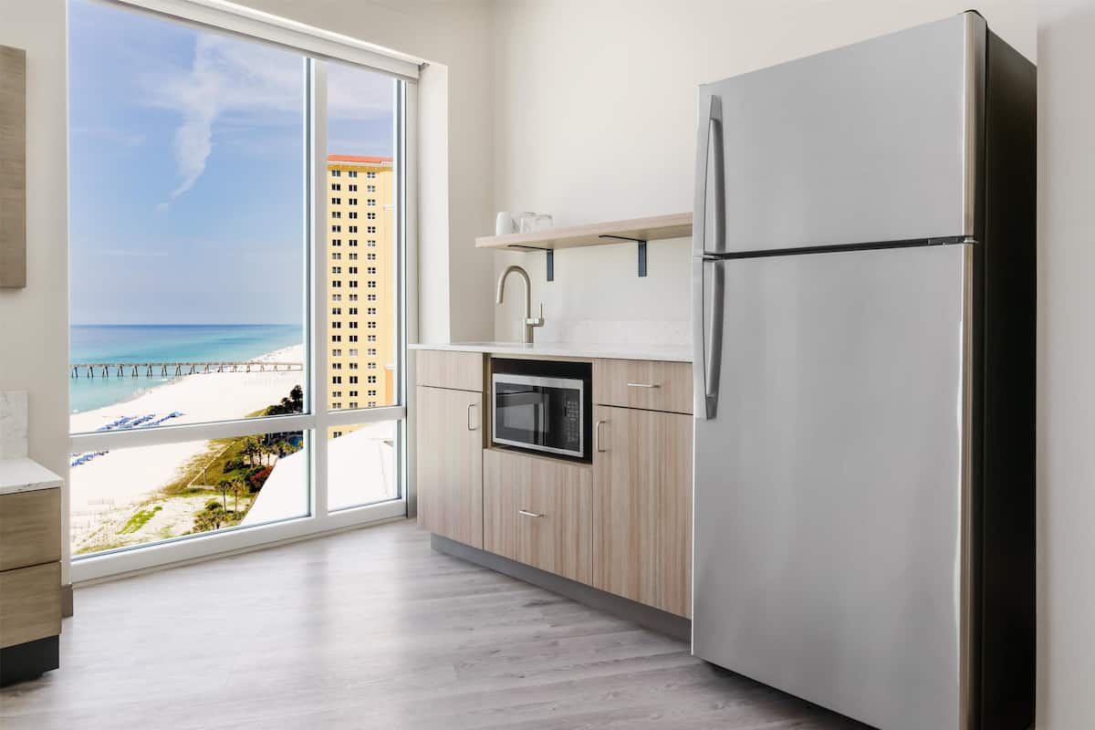 A modern kitchen with a view of the beach, a built-in oven, and a stainless steel refrigerator.