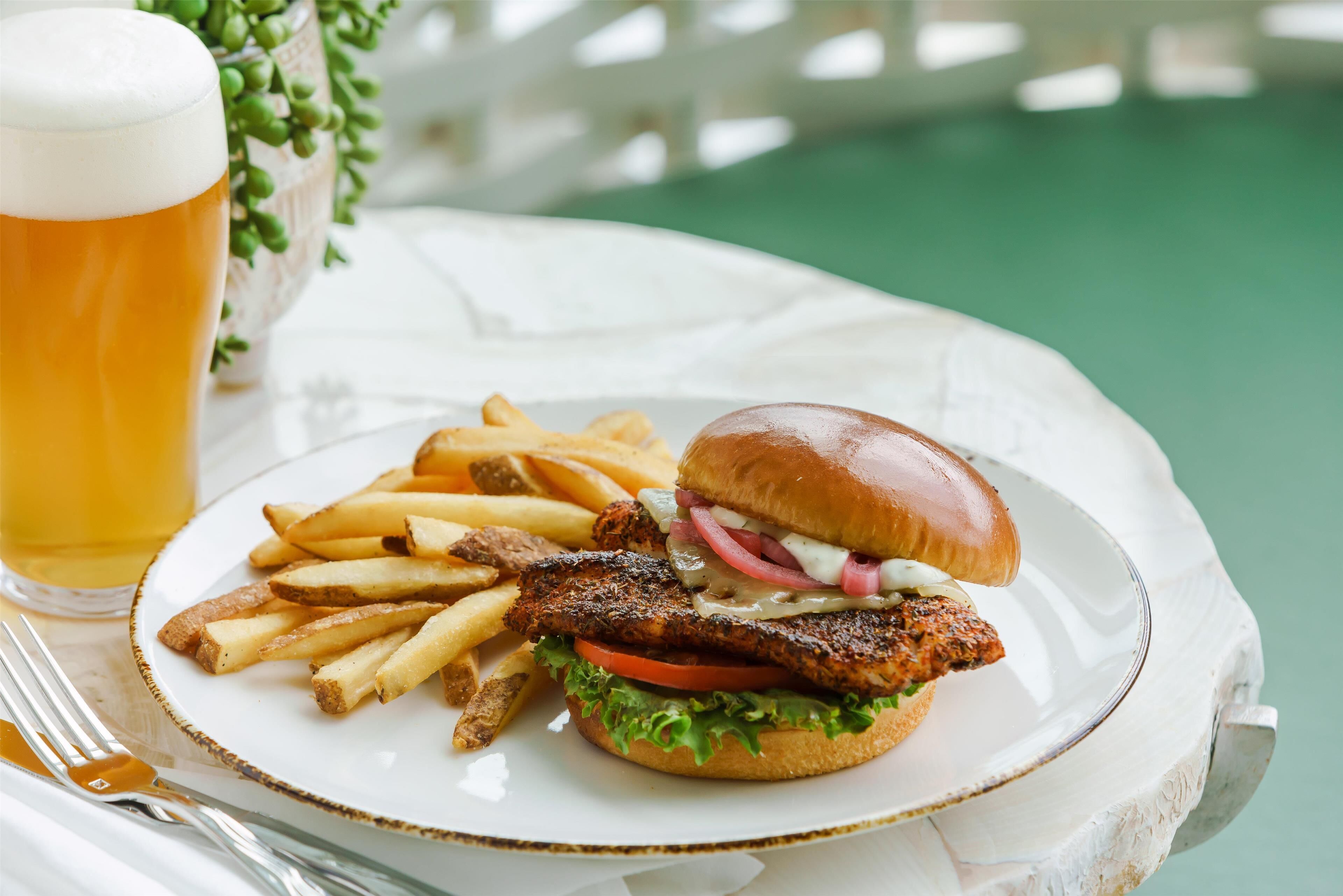 A plate with a burger, fries, and a glass of beer on a white table.
