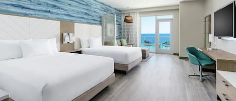 A hotel room with two beds, a desk, a chair, a TV, and a balcony with a view of the sea.