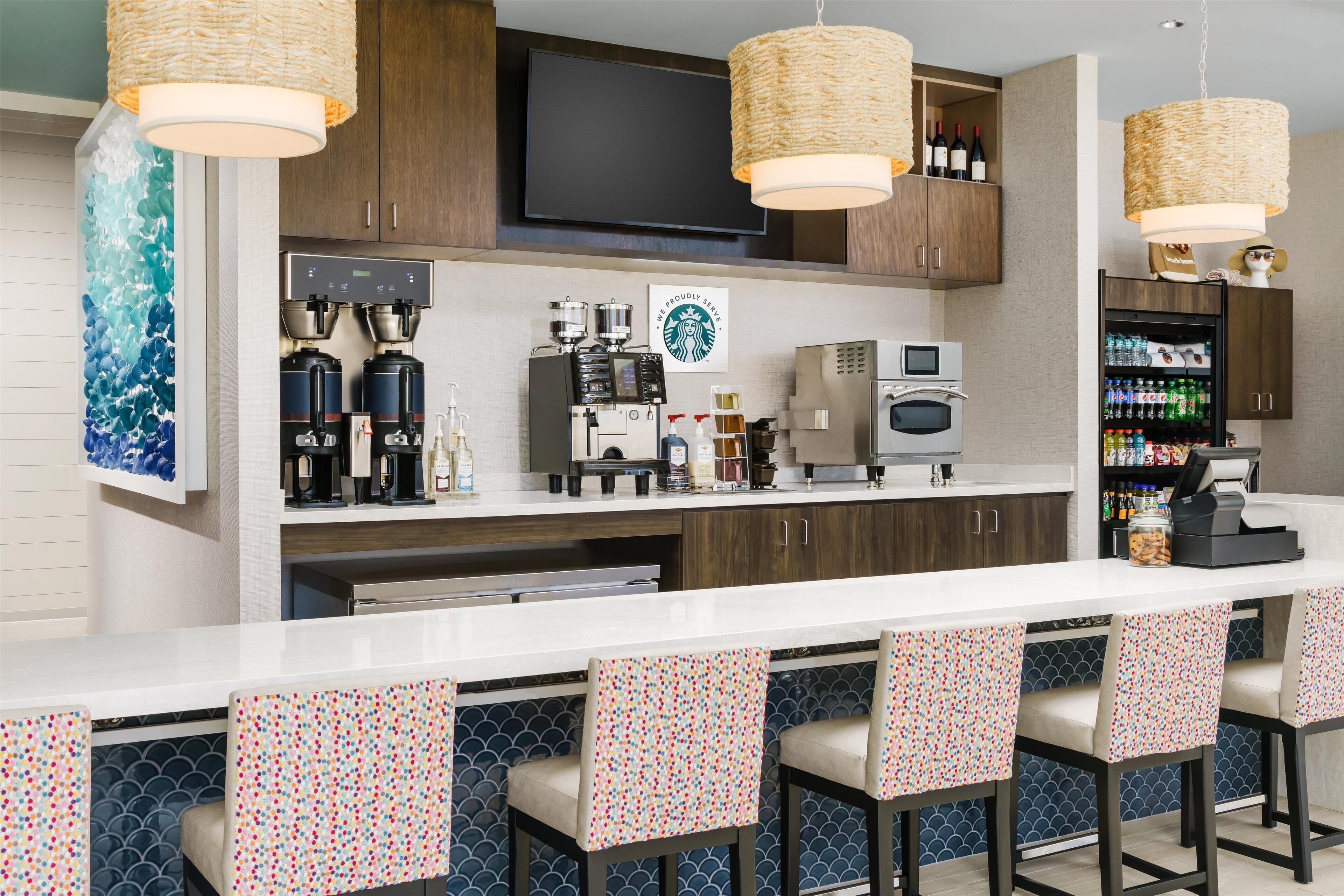 A modern kitchen with a long counter, bar stools, a coffee machine, and a refrigerator.