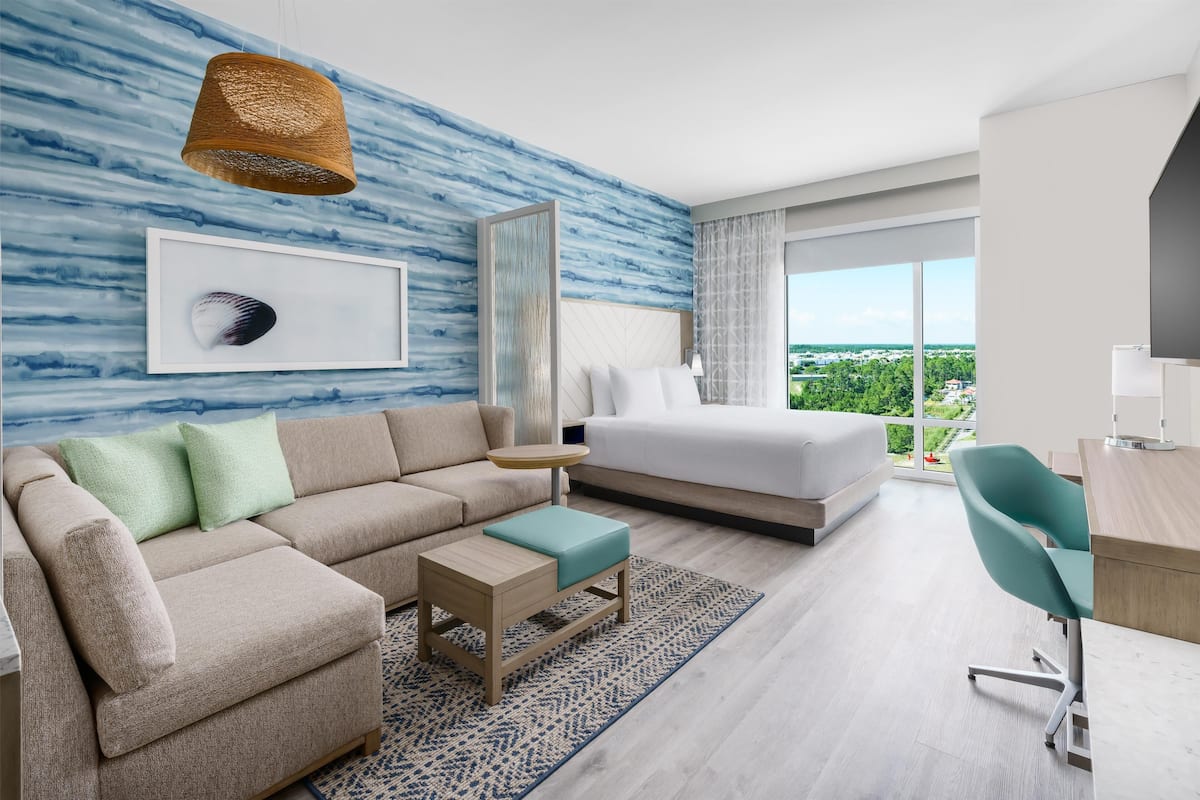 A modern hotel room with a large bed, a sofa, a desk, and a view of the city.