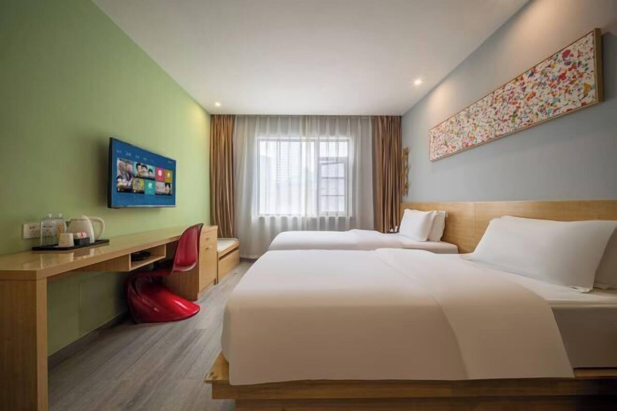 Hotelkamer met twee bedden, een bureau, een stoel, een televisie en een raam met gordijnen.