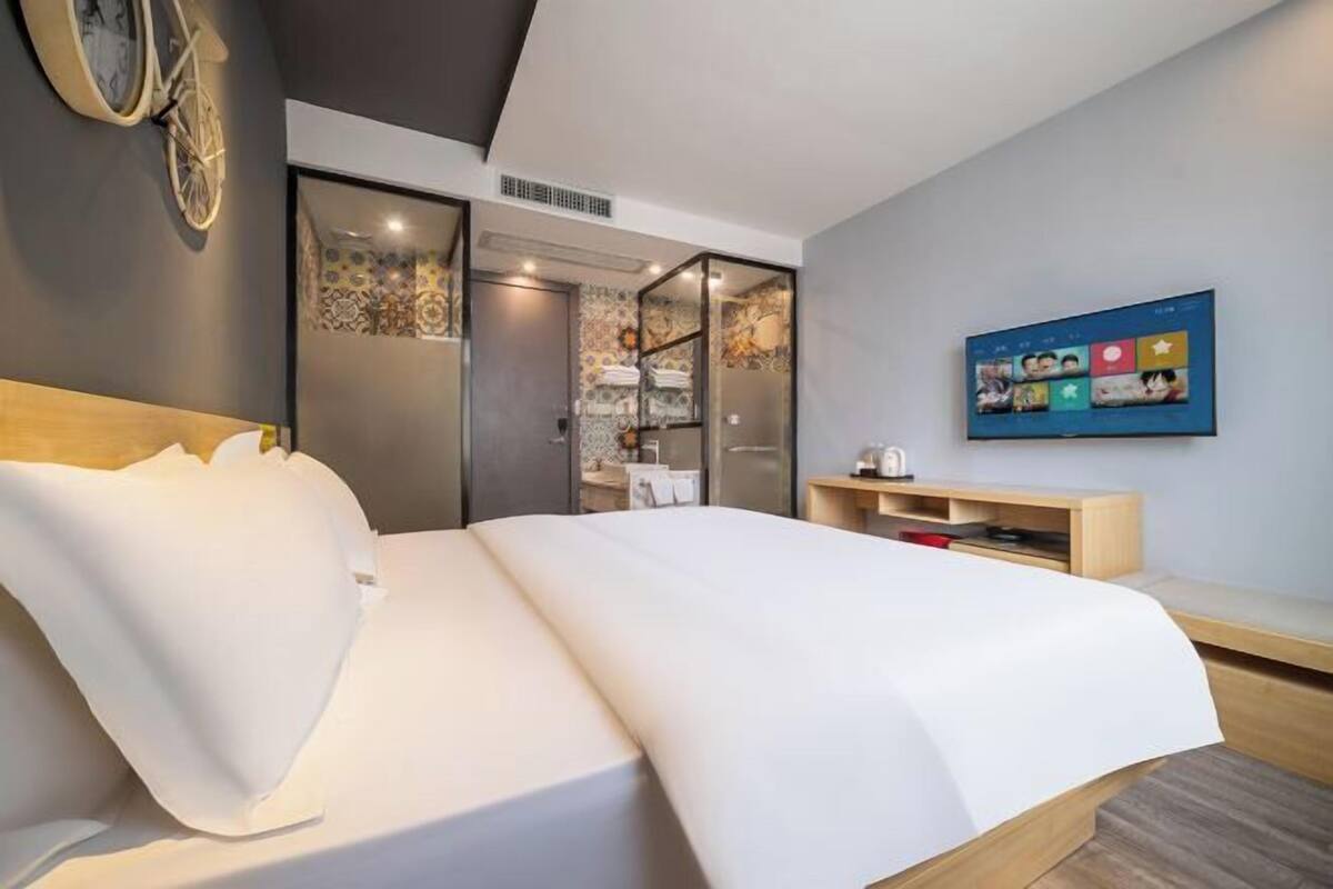 Een moderne hotelkamer met een groot bed, een houten hoofdeinde, een klein nachtkastje, een televisie en een kledingkast.