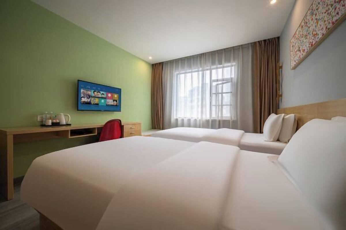 Een hotelkamer met twee bedden, een bureau met stoel, een televisie en een raam met gordijnen.