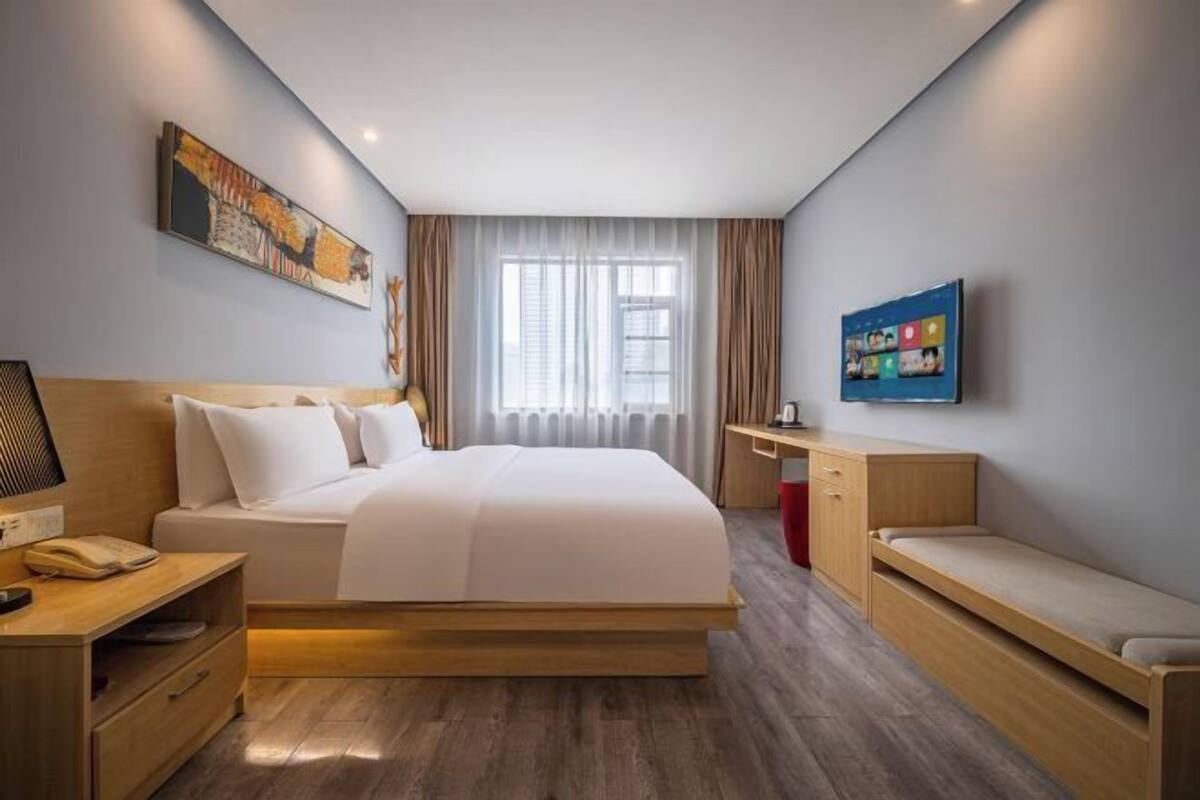 Een moderne hotelkamer met een groot bed, een bureau, een stoel, een televisie en een raam met gordijnen.