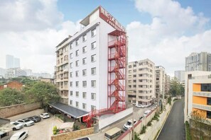 Ett hotell med flera våningar, en röd brandstege, en parkeringsplats och en omgivning som präglas av stadsmiljö.