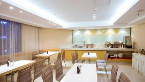 Un espace repas moderne avec des tables et des chaises, un comptoir équipé d’appareils de cuisine et une grande fenêtre agrémentée de rideaux.