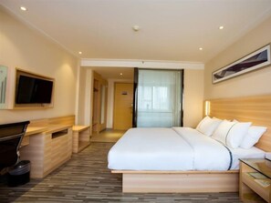 A hotel room with a bed, a desk, a television, and a door leading to another room. - City Comfort Inn (Guilin)