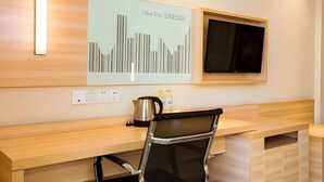 A modern hotel room with a wooden desk, a chair, a flat-screen TV mounted on the wall, and a decorative wall piece. - City Comfort Inn (Guilin)