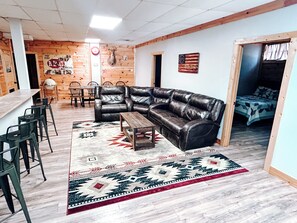 Een moderne woonkamer met een leren hoekbank, een houten salontafel en een vloerkleed met dessin. Er is een bar met krukken en een hangende lamp.