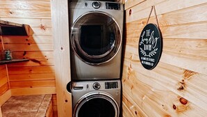 Une petite buanderie équipée de deux lave-linge à chargement frontal en acier inoxydable, avec des murs en bois et une petite étagère sur laquelle se trouve un récipient.
