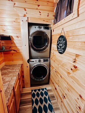 Een kleine wasruimte met twee wasmachines met voorlaadklep van roestvrij staal, houten wanden en een klein plankje met een bak.