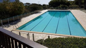 Une piscine rectangulaire à l’eau d’un bleu limpide, entourée d’une terrasse en pierre et d’une clôture en métal.