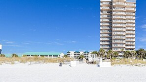 Um hotel alto, com vários andares e varandas, situado numa praia de areia com palmeiras.