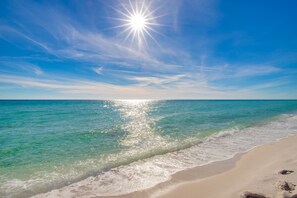 A beach with clear turquoise water, gentle waves, and a bright sun shining in the sky. - Beachfront condo with great gulf views, walk to Waterpark, Gigablast (Destin)