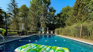 Ein Swimmingpool mit klarem, blauem Wasser, umgeben von einem Holenzaun und Bäumen.