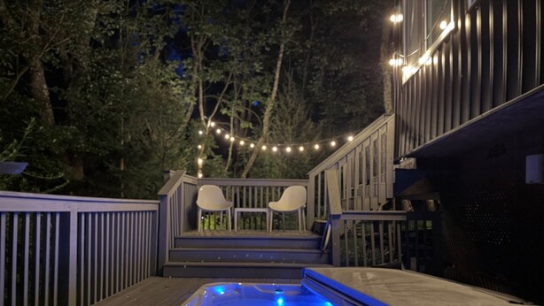 Ein Whirlpool auf einer Holzterrasse mit Geländer, umgeben von Bäumen und Lichterketten.