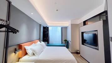 A modern hotel room with a large bed, a TV mounted on the wall, and a view of the city through the window.