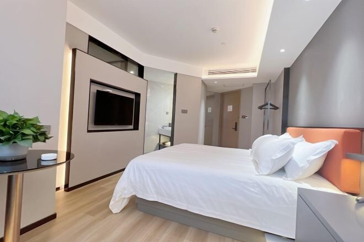 Una camera d'albergo moderna con un letto grande, una TV a parete, un comodino con una pianta e uno specchio.