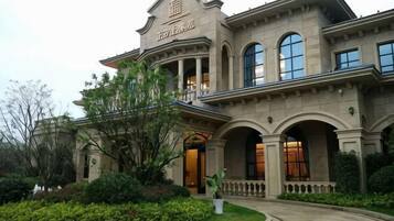 A large, historic building with a grand entrance, arched windows, and a well-maintained garden.