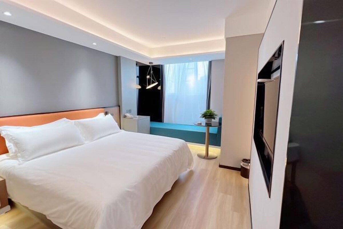Camera d'albergo moderna con un letto grande, una TV a parete e vista sulla città dalla finestra.