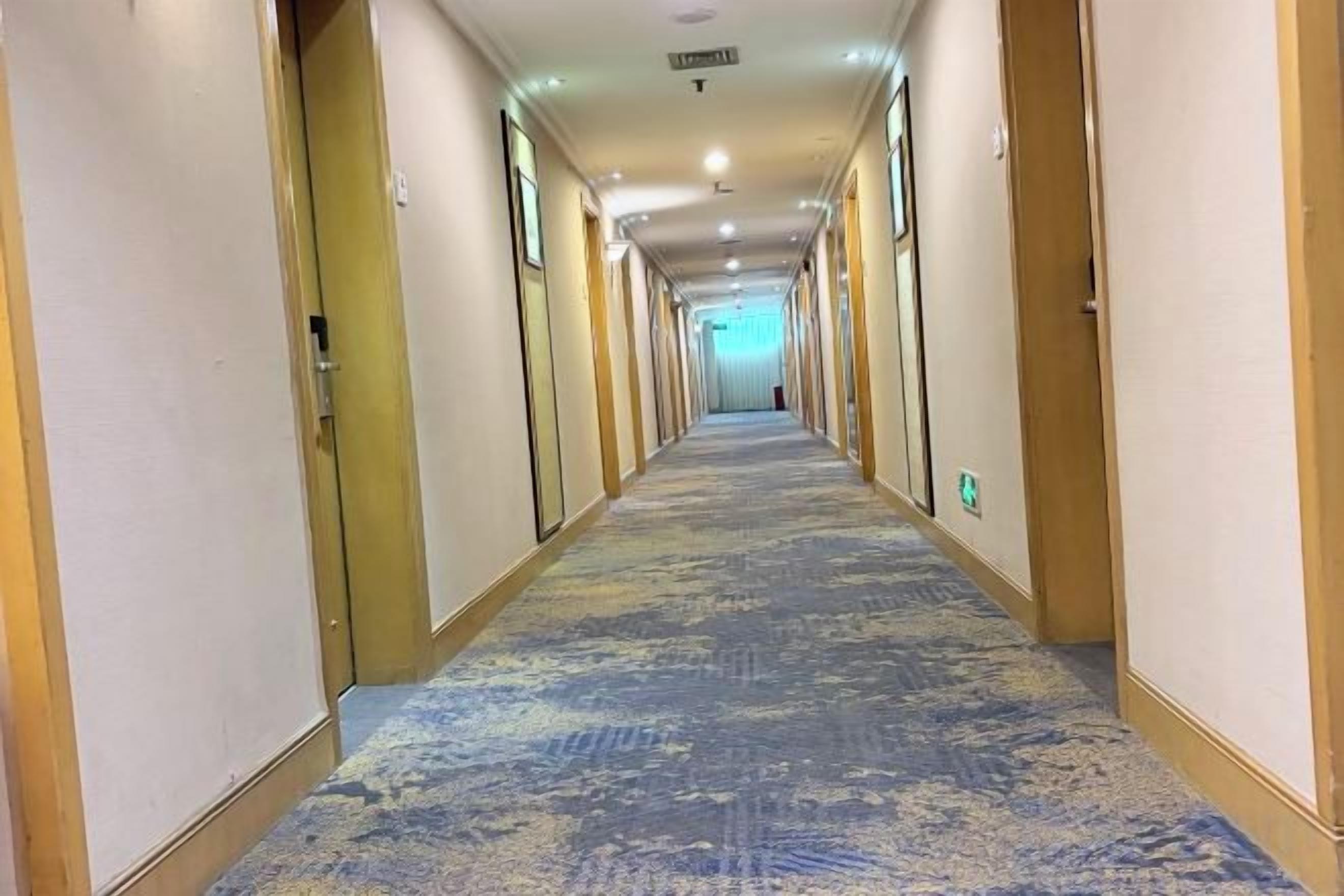 A hotel corridor with doors on both sides, carpeted floor, and a light at the end.