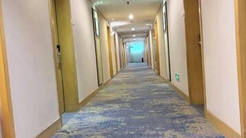 A hotel corridor with doors on both sides, carpeted floor, and a light at the end.