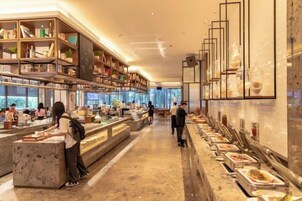 Un moderno vestíbulo de hotel con un mostrador de recepción alargado, una zona de buffet y un área de estar con mesas y sillas.