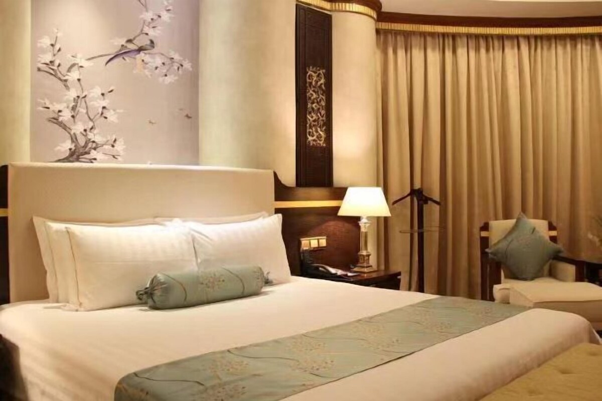 Une chambre d’hôtel avec un grand lit, une table de chevet avec une lampe, une chaise et un panneau décoratif au mur.