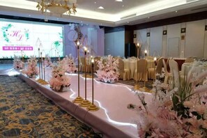 Une salle de banquet avec une scène, des tables dressées pour le repas et des décorations florales.