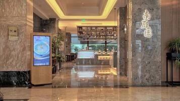 Een hotel lobby met een receptiebalie, een digitaal scherm en uitzicht op het restaurantgedeelte.