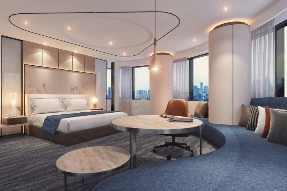 A modern hotel room with a bed, a round table, a sofa, and a city view.