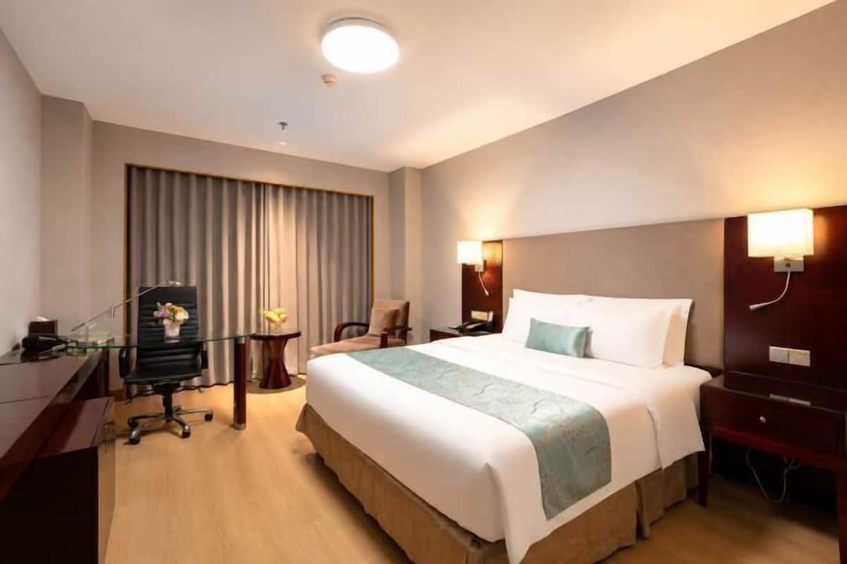 A hotel room with a bed, desk, chair, and a large window with curtains.