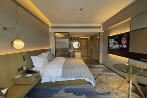 A modern hotel room with a large bed, a bedside table with a lamp, a TV mounted on the wall, and a patterned carpet. - Nanan Hotel (Nan'an)