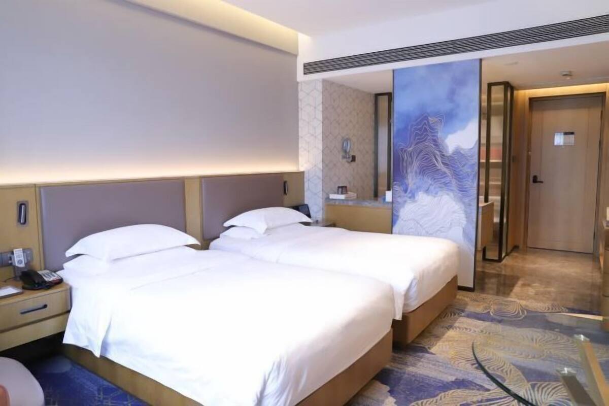A hotel room with two beds, a bedside table with a phone, a mirror, and a door leading to a bathroom.
